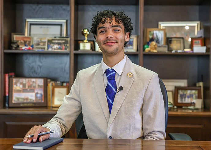 President for a Day winner Cristian St. Clair sits behind the desk of USD President James T. Harris III, DEd, on Wednesday, May 7, 2025. St. Clair, the current president of USD’s chapter of the National Society of Black Engineers, will graduate next weekend with a bachelor’s degree in computer science and a minor in visual arts. (Photo by Matthew Piechalak)