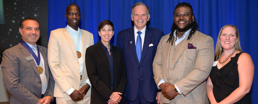 Alumni honorees standing on the Kroc IPJ stage with President Harris