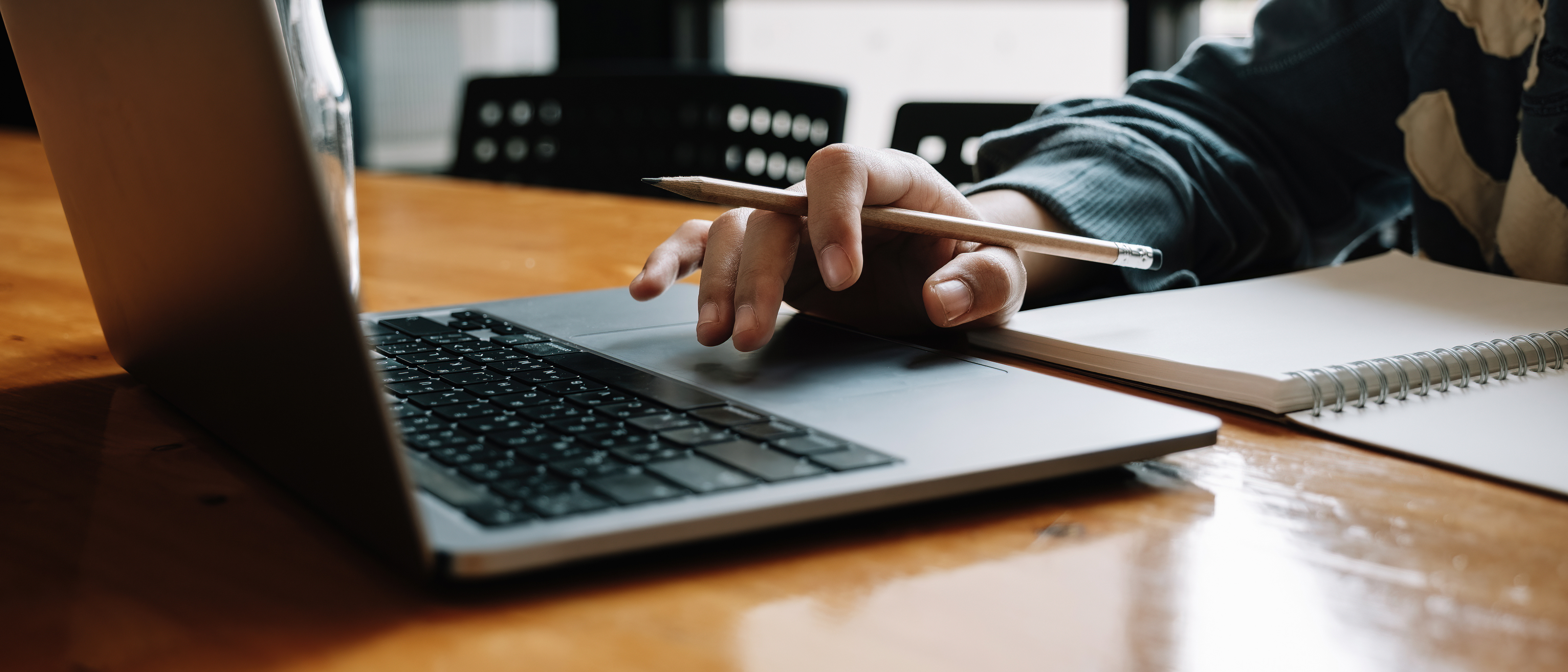 Person using laptop and taking notes in notepad while using laptop.