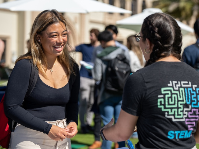 Two USD students are talking and smiling at each other on campus. 