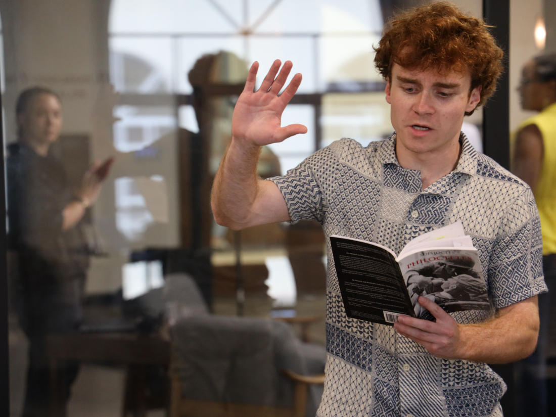 Student standing up and reading a book aloud for a theatre and political science class.