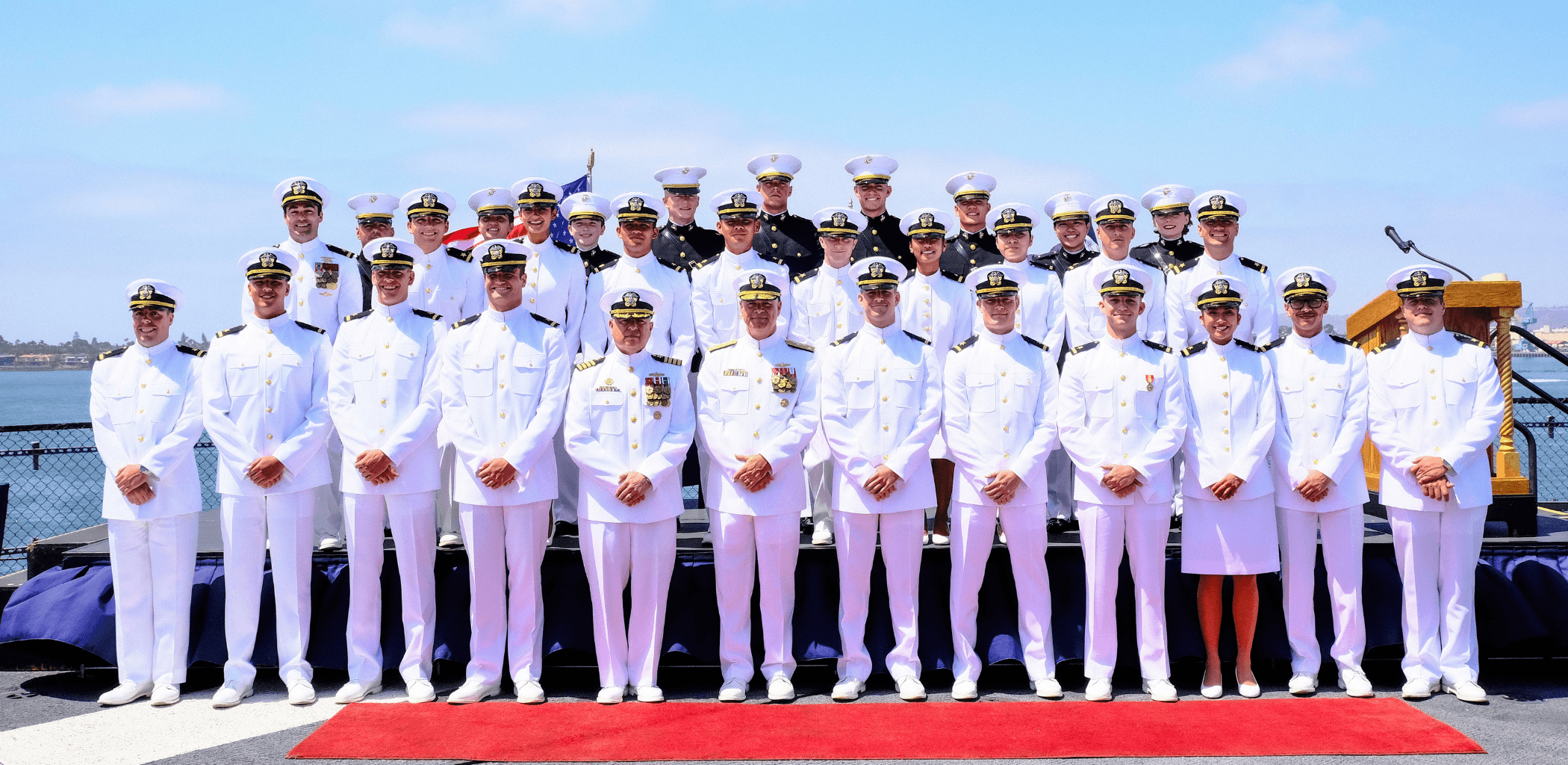 Twenty-nine newly commissioned ensigns and second lieutenants stand for a group photo aboard the USS Midway.