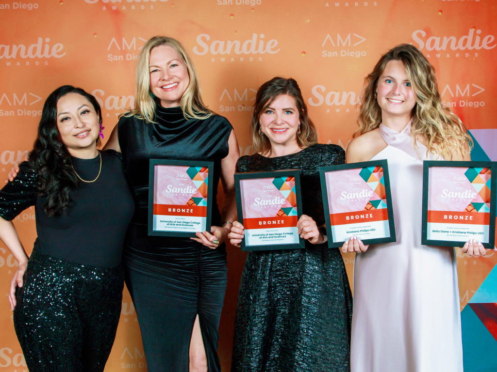 Gaby Ortiz Flores, Michelle Kennedy, Tanya Aubin and Kristi Phillips standing with their awards in front of an orange backdrop.