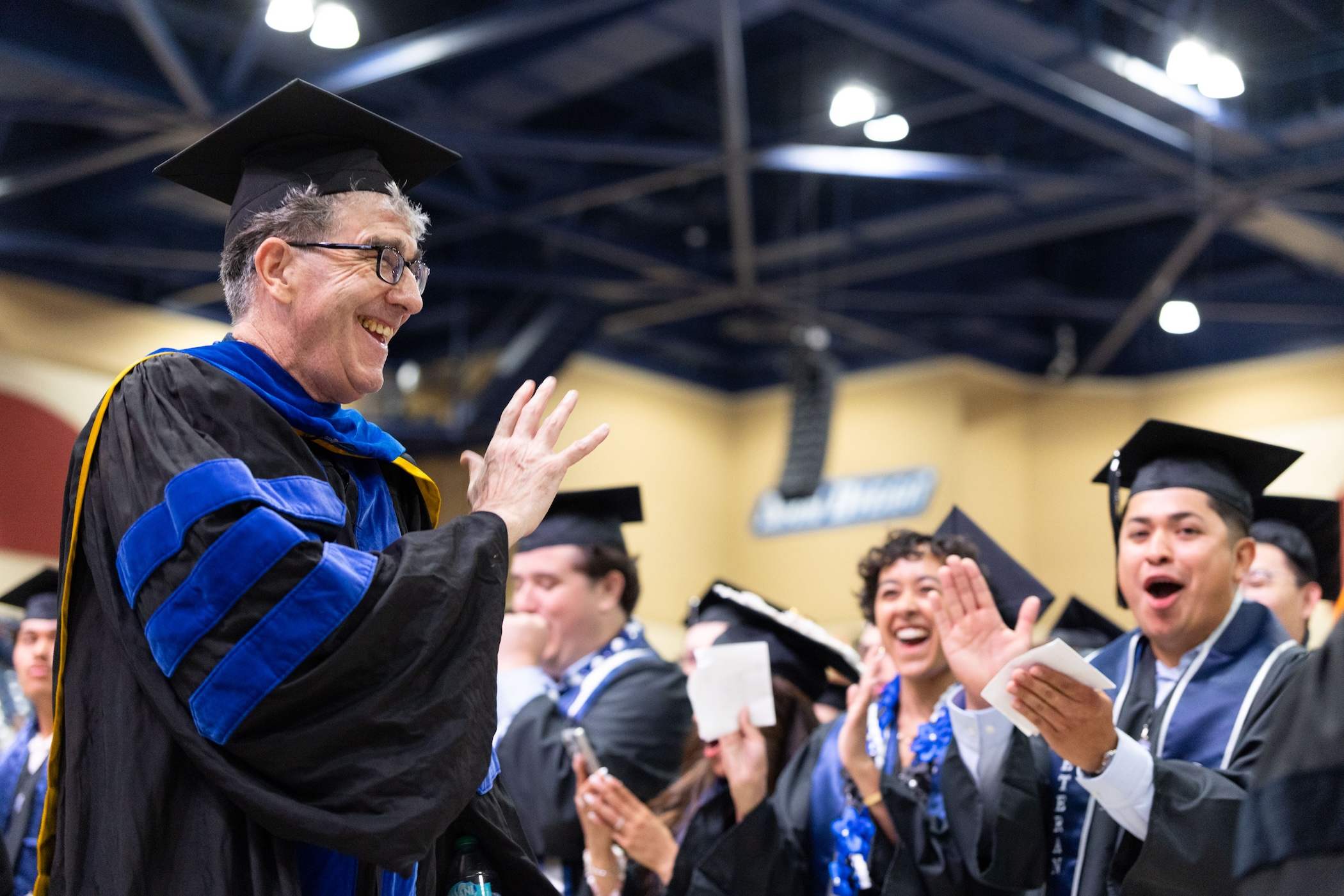 John Glick, PhD, waving at his students during the 2026 commencement ceremony