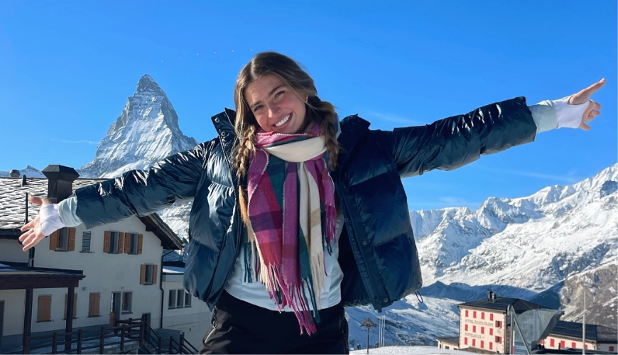 Tatum Tande stands with her arms extended and snow-covered mountains in the distance.