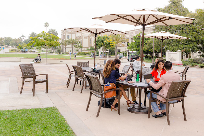 A group of 4 graduate business students sits at a table outside at the University of San Diego