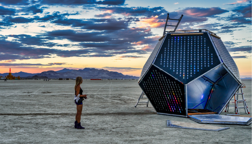 Professor and chair of mathematics Diane Hoffoss, PhD, stands in the desert of Black Rock City, Nevada, looking at ArtBuild's Unfolding Humanity as it's assembled at Burning Man.