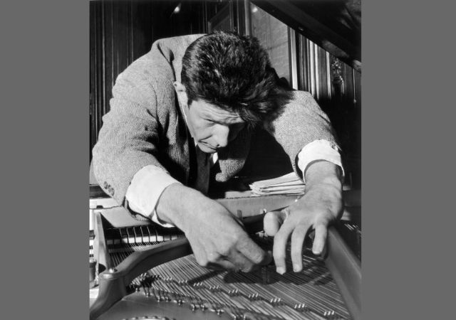 This is a black and white picture of John Cage playing an …
