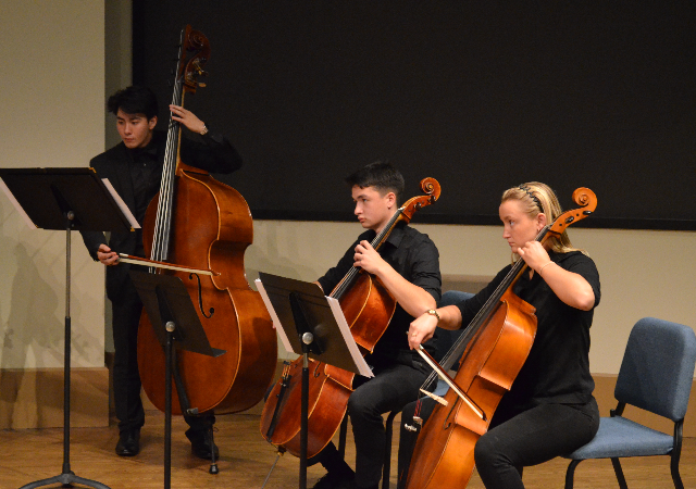 Two cellists and one bass student performing on stage.