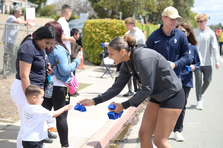 A USD student hands a cowbell to a parade attendee at the Linda Vista Multi-Cultural Fair and Parade (Photo: Lauren Radack)